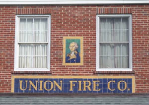 A painted portrait of George Washington mounted on the brick side wall of the Union Fire Co., above tiled lettering that reads UNION FIRE CO.